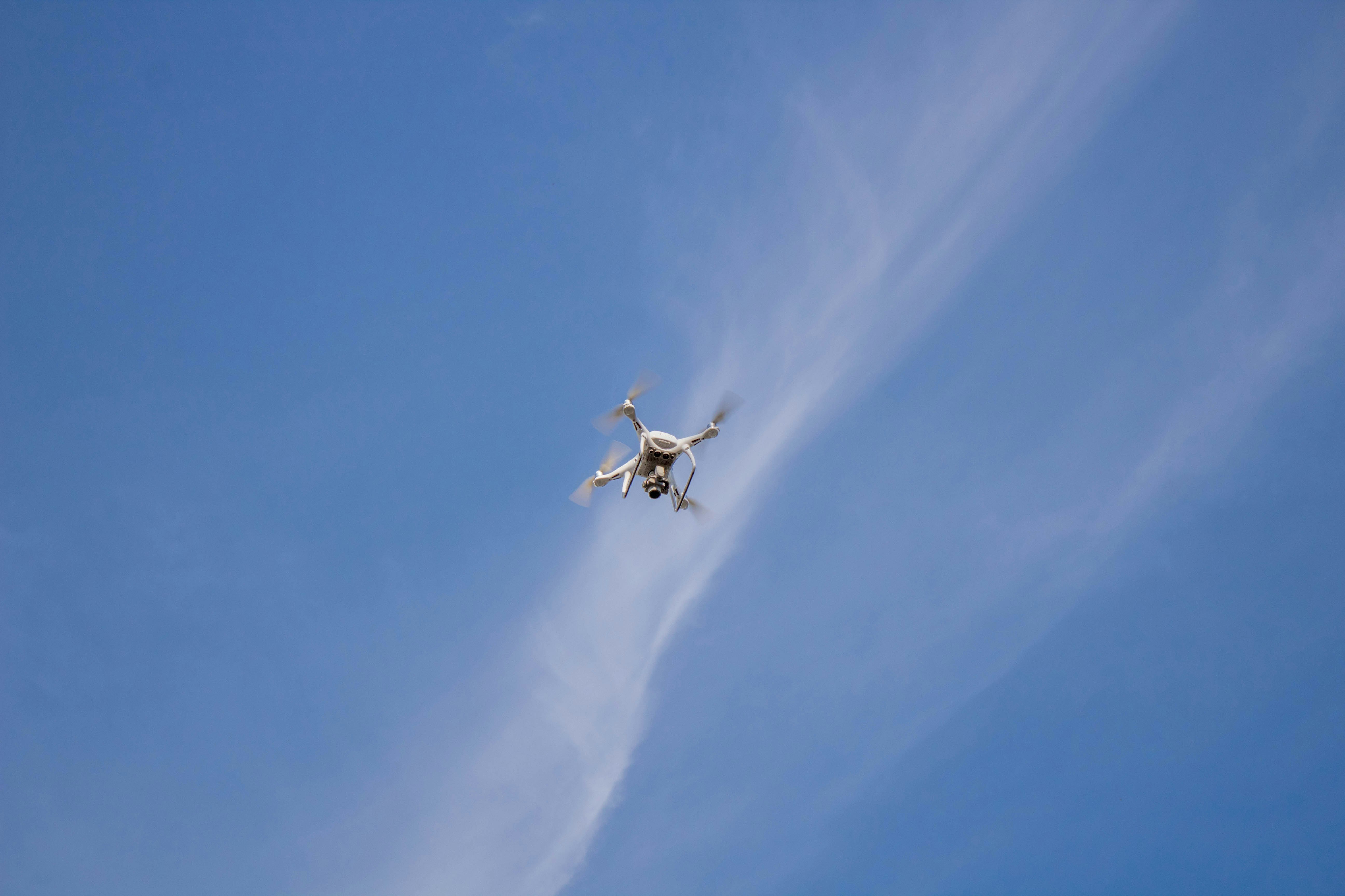 low-angle photography of flying white quadcopter drone at daytime